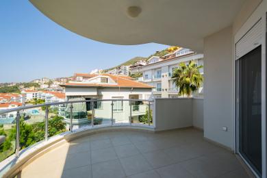 Şüşə məhəccərləri, kafel döşəməsi və ətrafdakı binaların mənzərəli görünüşləri olan parlaq Alanya balkonu.