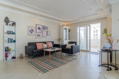 Salon w apartamencie w Alanyi z czarną skórzaną sofą, wzorzystym dywanem i jasną, przestronną atmosferą.