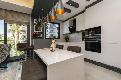 Alanya eiendom kjøkken med hvite skap, en quartz øy, pendelbelysning og en lys, moderne atmosfære.