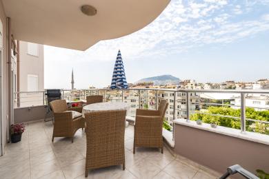 Balcone di proprietà ad Alanya con mobili in vimini, pavimento in piastrelle e vista sulla città sotto una luce naturale e brillante.