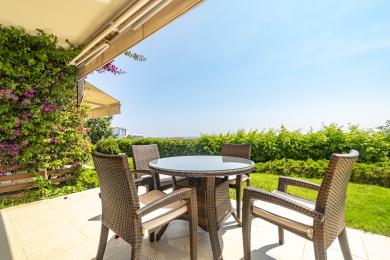 Balcón de propiedad en Alanya con muebles de mimbre, mesa de cristal, exuberante vegetación y un ambiente luminoso y soleado.