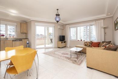Alanya'da balkon erişimi olan oturma odası, nötr tonlar, fayans zemin ve dekoratif Türk tarzı aydınlatma.