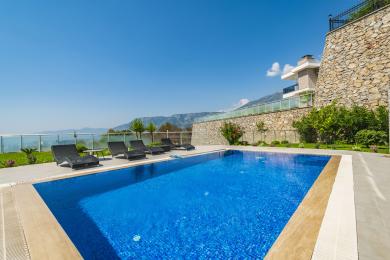 Alanya property featuring a luxurious outdoor pool with blue tiles, sun loungers, and stunning mountain views.