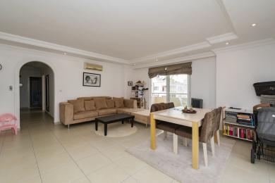 Ljust vardagsrum i Alanya med en beige sektionssoffa, matbord och klinkergolv, vilket skapar en bekväm atmosfär.