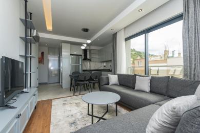 Das Wohnzimmer der Alanya Immobilie verfügt über eine moderne Küche, ein graues Sofa und helles, natürliches Licht durch große Fenster.