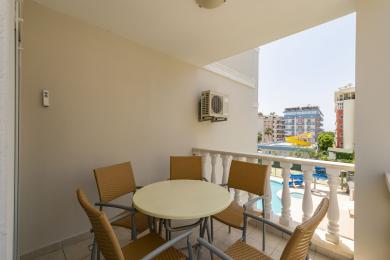 Balkon nekretnine u Alanji sa stolicama od pruća, okruglim stolom i svijetlim, sunčanim pogledom na bazen.