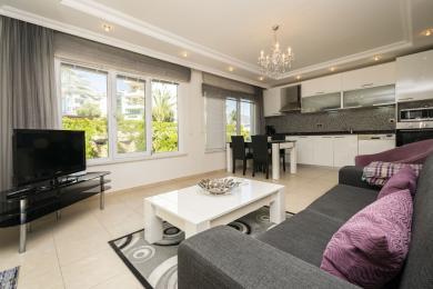 Alanya Immobilie: Heller, offener Wohnbereich mit moderner, weißer Küche, Fliesenböden und großen Fenstern mit Blick ins Grüne.