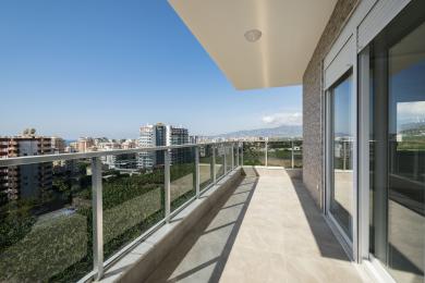 Balkon nekretnine u Alanji sa staklenim ogradama, podovima od pločica i panoramskim pogledom na grad i planine.