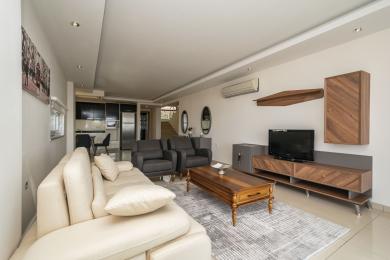 Le salon lumineux d'Alanya comprend un canapé crème, des fauteuils gris, des meubles en bois et une cuisine américaine.