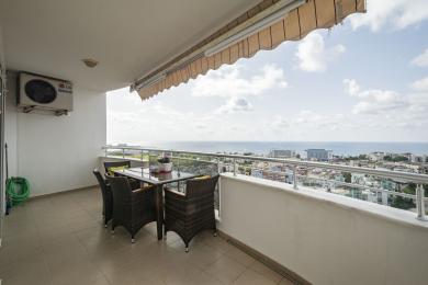 Balcón de propiedad en Alanya con muebles de mimbre, suelo de baldosas e impresionantes vistas al mar bajo una luz natural brillante.