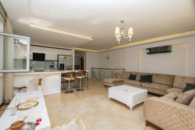 Propriedade em Alanya: Sala de estar luminosa e em plano aberto com cozinha moderna, sofá bege e piso de cerâmica polida.