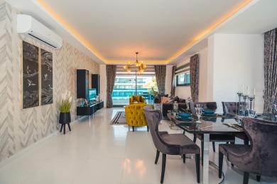 Nemovitost Alanya: Světlý, otevřený obývací a jídelní prostor s moderním nábytkem, přístupem na balkon a teplým ambientním osvětlením.