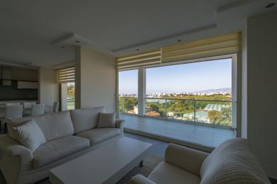 Sala de estar luminosa em Alanya com sofás brancos, uma varanda e vistas panorâmicas da cidade.