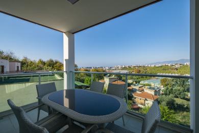 Varanda de propriedade em Alanya com móveis de vime, grades de vidro e vistas panorâmicas da cidade e da paisagem.