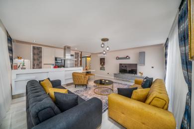 Propriété à Alanya : Salon lumineux et moderne avec cuisine ouverte, canapés élégants et éclairage contemporain créant une atmosphère confortable.