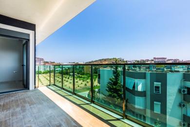 Balkon nekretnine u Alanji sa staklenom ogradom, podom od pločica i svetlim, sunčanim pogledom.