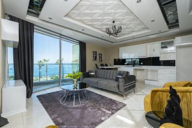 Propriété à Alanya : Salon lumineux et moderne avec vue sur l'océan, comprenant des armoires blanches élégantes et un canapé gris moelleux.