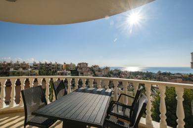 Balkon nekretnine u Alanji s namještajem od pruća nudi zadivljujući pogled na more pod vedrim, sunčanim nebom.