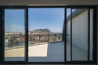 Un balcone luminoso ad Alanya con ringhiere in vetro offre viste mozzafiato sulla città e sul mare attraverso grandi porte scorrevoli in vetro.