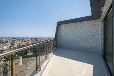 Balcone di proprietà ad Alanya con ringhiere in vetro, pavimenti in piastrelle, parete a mosaico e vista panoramica sulla città e sul mare.
