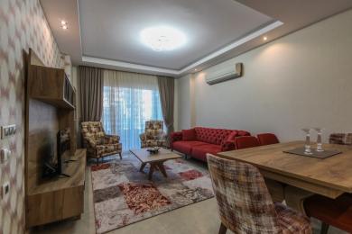 Salon de propriété à Alanya avec un canapé rouge, des chaises à motifs et un éclairage vif et accueillant.