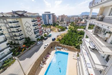 Vista da propriedade de Alanya mostrando uma piscina azul brilhante e edifícios circundantes em um dia ensolarado.