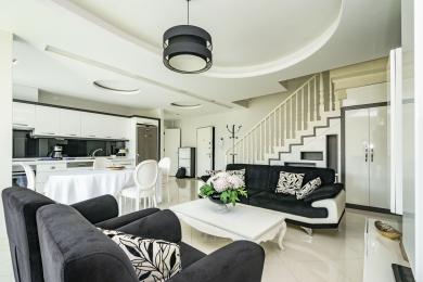 Salon lumineux et ouvert d'Alanya avec cuisine blanche moderne, escalier et mobilier élégant en noir et blanc.