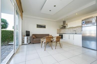 Lichte Alanya appartement woonkamer met witte tegelvloeren, een moderne keuken en toegang tot een balkon, wat een verfrissende sfeer creëert.