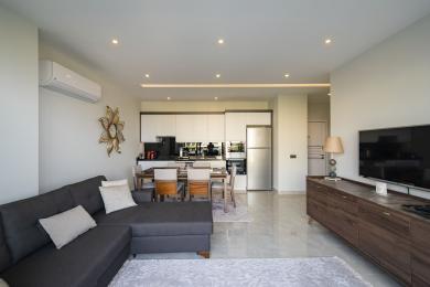 Il soggiorno di questa proprietà di Alanya presenta una cucina moderna, zona pranzo, divano grigio e tonalità chiare e neutre.