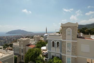 Deze woning in Alanya biedt een prachtig uitzicht op de stad, de zee en de bergen vanaf de met steen geaccentueerde, lichte balkons.