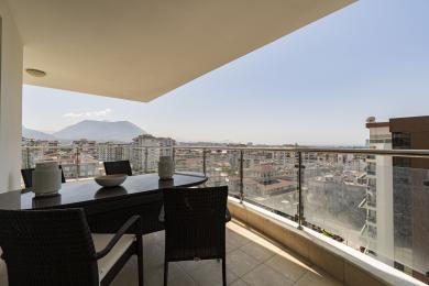 Alanya-Immobilienbalkon mit Glasgeländern, Korbmöbeln und Panoramablick auf Stadt und Berge.