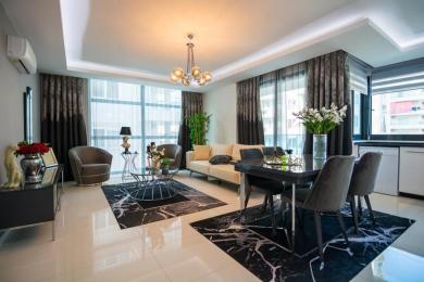 Alanya onroerend goed woonkamer met een moderne kroonluchter, marmeren vloerkleden en kamerhoge ramen met transparante gordijnen.