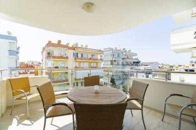 Alanya kinnisvara rõdu vitspunutud mööbli, klaaspiirete ja ereda päevavalgusega, vaatega linnale.