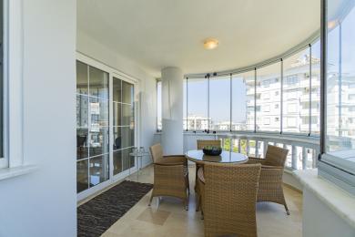 Светол балкон во Алања со мебел од ратан, стаклени ѕидови кои нудат поглед на градот и под од светол мермер.