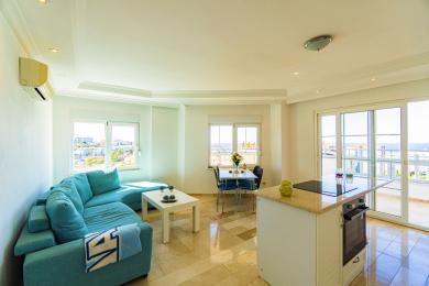 Lichte Alanya appartement woonkamer met turquoise sofa, marmeren vloeren en uitzicht op zee vanaf het balkon.