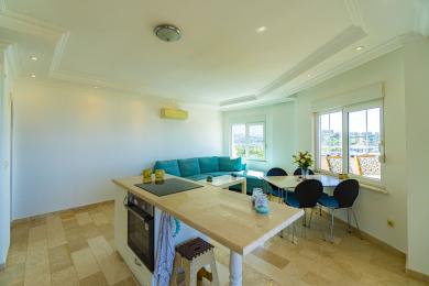 Área de estar luminosa do apartamento em Alanya com cozinha moderna, sofá turquesa e vistas panorâmicas.