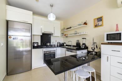 Cozinha de propriedade em Alanya com armários brancos, bancadas de granito preto, eletrodomésticos de aço inoxidável e iluminação brilhante e convidativa.