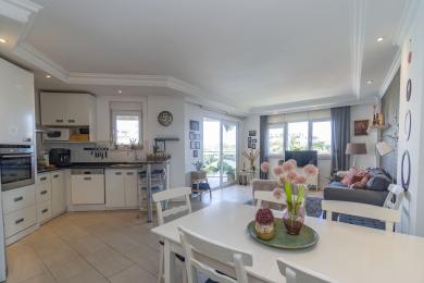 Helle, offen gestaltete Alanya-Wohnung mit einer modernen weißen Küche, einem Essbereich und einem Wohnzimmer mit Zugang zum Balkon.