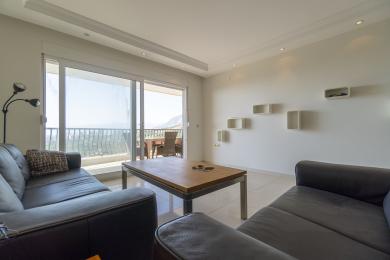 Bright Alanya living room featuring leather sofas, a wood table, balcony access, and minimalist white wall shelves.