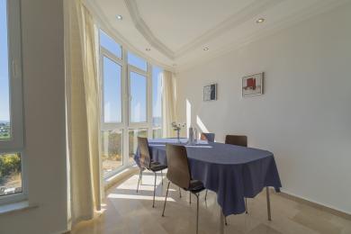 Heller Alanya-Esszimmer mit großen Fenstern, Marmorböden und einem blau gedeckten Tisch, der eine heitere Atmosphäre schafft.