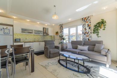 A área de estar luminosa deste apartamento em Alanya apresenta uma cozinha moderna, assentos confortáveis e luz natural entrando pelas grandes janelas.