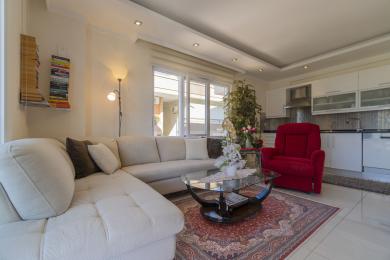 Lichte Alanya woonkamer met een witte bank, rode fauteuil en moderne open keuken.