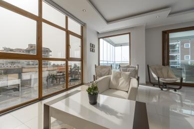 Lys Alanya stue med store vinduer, hvite fliser, moderne møbler og en avslappet, luftig atmosfære.
