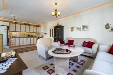 Alanya onroerend goed woonkamer met een marmeren tafel, crèmekleurige banken en een open keuken met warme verlichting.