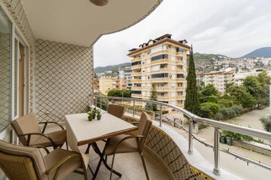 Proprietate în Alanya cu balcon cu pereți cu gresie, balustrade metalice și scaune de exterior cu vedere spre oraș.