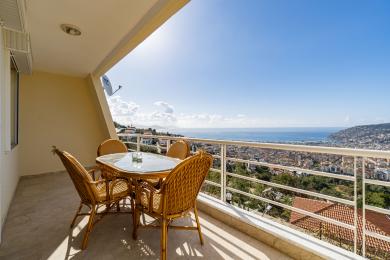 Balkon nemovitosti v Alanyi s proutěným nábytkem, dlažbou a úžasným panoramatickým výhledem na moře a město.