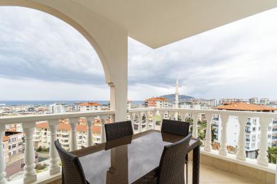 Alanya eign með svölum með húsgögnum úr víð og víðáttumikið útsýni yfir borgina og sjóinn undir skýjuðum himni.