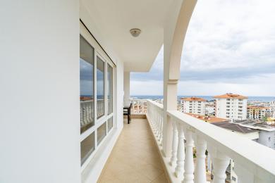 Balcone di una proprietà ad Alanya con balaustra bianca, pavimento in piastrelle e vista sulla città sotto un cielo nuvoloso.