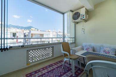 Svijetli, zatvoreni balkon u Alanji s pogledom na grad, s podovima od pločica, udobnim sjedalima i puno prirodnog svjetla.