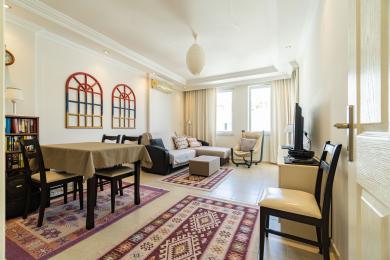 Svijetli dnevni boravak apartmana u Alanji s podovima od pločica, udobnim sjedećim garniturama, blagovaonicom i ukrasnom zidnom umjetnošću u stilu prozora.